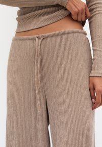 Pantalon en maille côtelée beige avec une taille à cordon et des jambes larges, présentant une texture douce et une coupe décontractée.