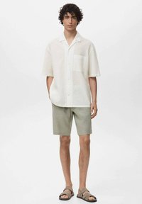 Korte mouwen witte shirt van een gestructureerde stof, gecombineerd met lichtgroene shorts en bruine sandalen. Voorzien van een borstzak en een relaxte pasvorm.