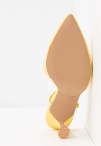 Chaussure à talons hauts jaune avec un embout pointu et une texture lisse. La semelle est marron clair avec de fines rainures et un petit talon.