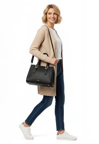 Kobieta idąca, ubrana w beżowy kardigan, białą koszulę, niebieskie dżinsy, białe trampki, niosąca czarną, teksturowaną torebkę z paskami przewieszoną przez ramię.