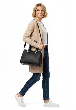 Kobieta idąca, ubrana w beżowy kardigan, białą koszulę, niebieskie dżinsy, białe trampki, niosąca czarną, teksturowaną torebkę z paskami przewieszoną przez ramię.