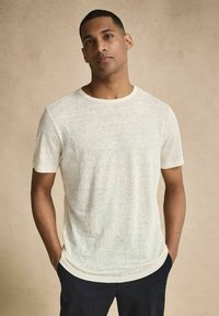 Lyse beige kortærmet T-shirt lavet af blødt, struktureret stof med rund halsudskæring og en subtil meleret mønster, båret med hænderne i lommerne.