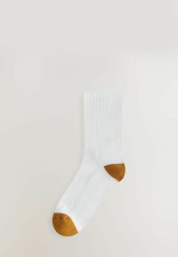 Calzino bianco di cotone con texture a coste, dotato di un tallone e una punta in contrasto marrone. Il design è di lunghezza media fino al polpaccio.