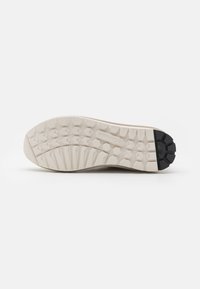 Semelle de chaussure beige clair en caoutchouc texturé pour une meilleure adhérence, présentant un motif hexagonal et des accents en caoutchouc foncé au niveau du talon.