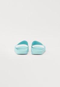 Et par turkise flip-flops med flate såler og brede stropper, som har en glatt tekstur og åpen bakdesign.
