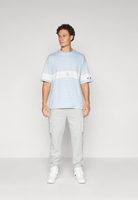 Lyseblå stribet t-shirt lavet af bomuld, med rund hals og logo på forsiden, kombineret med grå sweatpants og hvide sneakers.