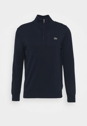 Marinblå tröja med hög krage och halvdragkedja. Gjord av mjukt material, med en liten grön krokodil-logga på bröstet.