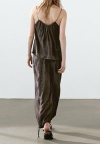 Ensemble sombre en deux pièces comprenant un haut sans manches avec un dos froncé et un pantalon ample avec des ourlets à cordon de serrage, le tout en tissu texturé.