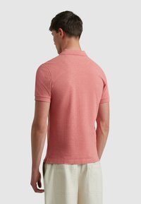 Roze gemêleerde polo met een kraag, korte mouwen en zijsplitten, gecombineerd met crèmekleurige shorts. Zacht, gestructureerde stof.