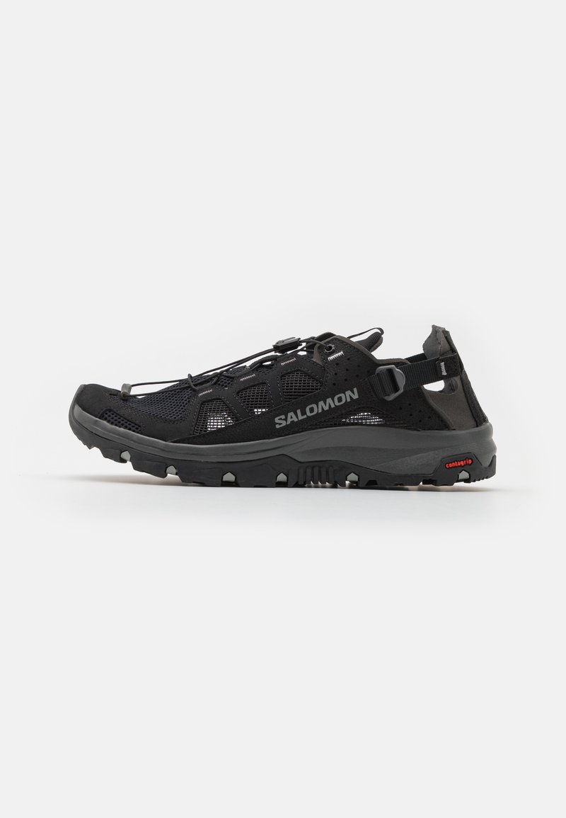 Black mesh hiking shoe with textured rubber sole, adjustable lacing system, and bold branding. Features a back heel strap for support.