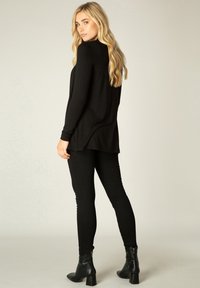Zwarte langemouwen top met een ontspannen pasvorm, gecombineerd met zwarte getailleerde broeken en zwarte enkellaarsjes met een blokhak. Glad, stretchy materiaal.