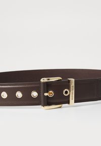 Bruine leren riem met een goudkleurige gesp, voorzien van metalen oogjes en stikdetails. Eenvoudig, breed ontwerp voor een veilige pasvorm.