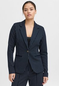 Blazer bleu marine à rayures, fabriqué en tissu texturé avec un design ajusté, des revers en dents de scie, une fermeture à un bouton et deux poches avant.