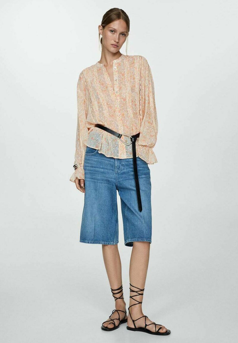 Bloemige, langemouwen, lichtoranje blouse met knoopsluiting, gecombineerd met blauwe denim short en zwarte sandaaltjes met banden.