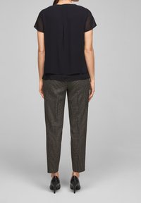 Blusa nera trasparente a maniche corte, sovrapposta a un top uniforme, abbinata a pantaloni attillati a righe nere e bianche e tacchi alti neri.