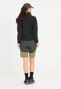 Svart huvtröja med texturerade ärmar, grå och olivgröna shorts, samt svarta vandringsskor. En keps fulländar den sportiga outfiten.