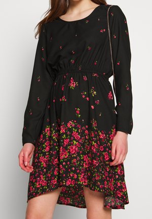 Sort langærmet kjole med indsnørret talje, med et rødt og grønt blomsterprint koncentreret på skørtet og spredt på toppen.
