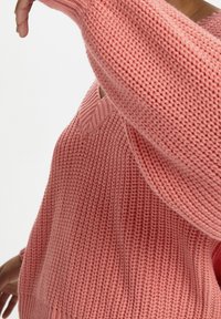 Maglione rosa lavorato a maglia con motivo a coste testurizzato e scollo a V. Presenta maniche lunghe e vestibilità comoda.