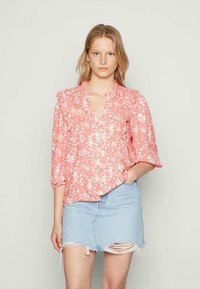 Blusa floral rosa com padrões brancos, detalhes franzidos na frente e nas mangas, combinada com uma saia de jeans desgastada em azul claro.