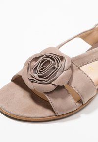 Beżowe zamszowe sandały z warstwowym akcentem kwiatu na pasku, otwarty nosek oraz wycięte boki dla wentylacji.
