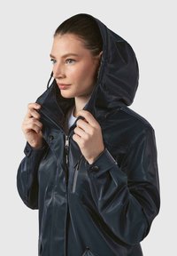 Marineblå vandtæt jakke med hætte, lynlåslukning foran og trykknapmanchetter; blank finish og to frontlommer.