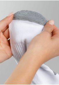 Hvid sok med en struktureret grå krave holdes af to hænder. Sokken har ribbet detaljer ved åbningen og et blødt stof.
