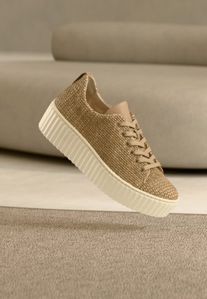 Beige színű, szőtt sportcipő texturált felsőrésszel, világosbarna bőrácskásokkal és fehér, bordázott talppal, semleges háttér előtt bemutatva.