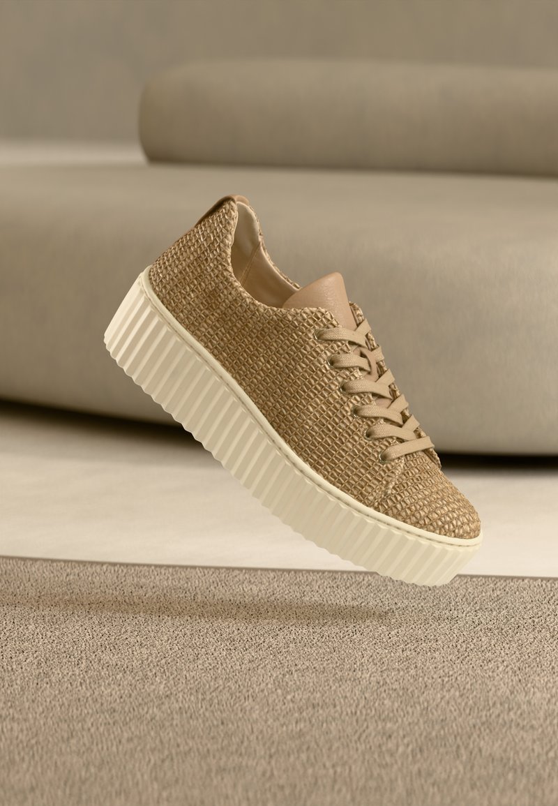 Μπεζ πλεκτό αθλητικό παπούτσι με υφή στο πάνω μέρος, αξεσουάρ από ταμπά δέρμα και λευκή ραβδωτή σόλα, απεικονισμένο πάνω σε ουδέτερο φόντο.