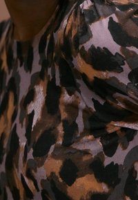 Tessuto leopardato marrone e nero con una texture liscia e una leggera lucentezza, caratterizzato da dettagli con maniche a sbuffo e una silhouette aderente.