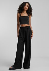 Top corto nero con scollatura quadrata abbinato a pantaloni larghi a vita alta. Tessuto liscio, design minimale e vita elastica.