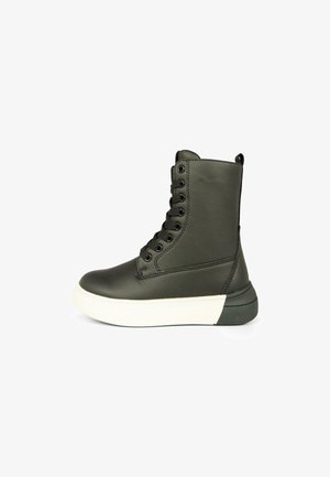 Zwarte leren enkelboot met een witte rubberen zool, ronde neus en acht veterogen. Beschikt over een achterste treklip en een gestructureerd oppervlak.