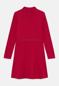 Robe rouge à manches longues avec un col, présentant une subtile touche de paillettes à la taille et une coupe droite, fabriquée en tissu doux et extensible.