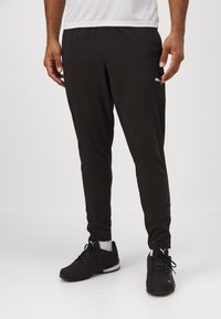 Zwarte sportbroek met een taps toelopend ontwerp, gemaakt van lichtgewicht stof. Kenmerkt zich door een klein wit logo op de linkerdij en een elastische tailleband.