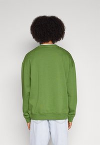 Felpa verde con una vestibilità comoda, colletto rotondo e polsini a costine. Il tessuto appare morbido e con una texture liscia; non presenta motivi.