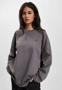 Long-sleeve gray sweatshirt made of soft fabric. Features a small logo on the chest and a relaxed fit with dropped shoulders.