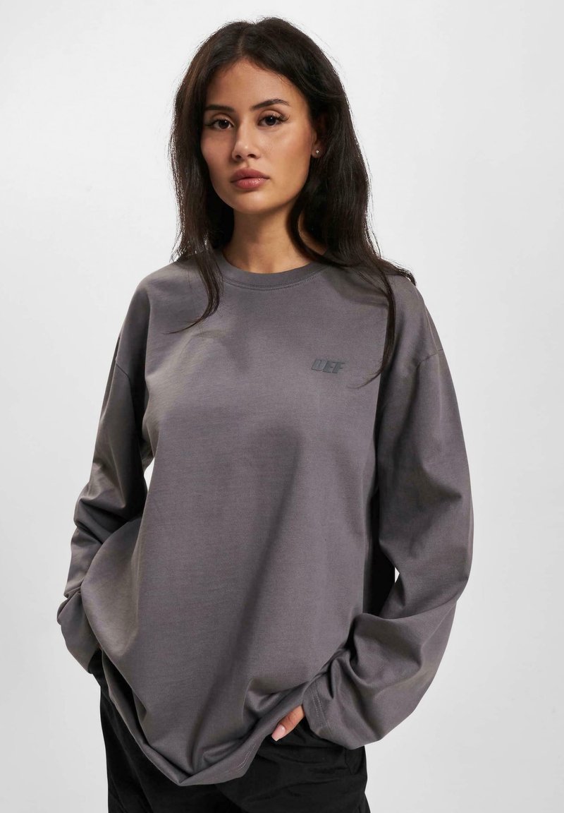 Long-sleeve gray sweatshirt made of soft fabric. Features a small logo on the chest and a relaxed fit with dropped shoulders.