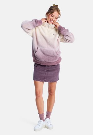 Fleece pullover in cream to lavender ombre, with a half-zip, large front pocket, and cuffed sleeves. Paired with a purple corduroy skirt.