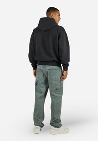 Zwarte hoodie met een grote capuchon, gecombineerd met lichtblauwe cargobroek met meerdere zakken en een relaxte pasvorm, gedragen met witte schoenen.