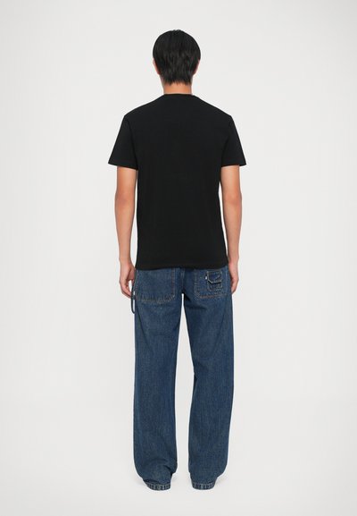 T-shirt en coton noir avec un col rond, associé à un jean bleu délavé à coupe ample, comportant une poche arrière et des détails de couture visibles.
