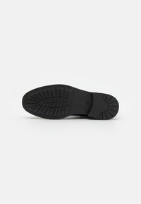 Black rubber shoe sole with a textured grip pattern, featuring a rounded toe and flat design. Durable material for traction and stability.