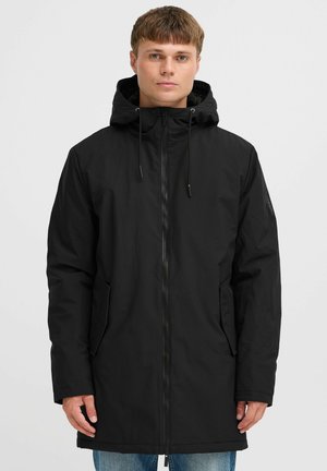 Parka negra larga con cremallera frontal, capucha ajustable y dos bolsillos laterales. Presenta un ligero brillo y una textura suave.