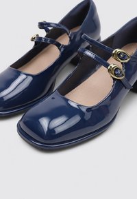 Zapatos de charol azul marino con punta cuadrada, dos correas ajustables y botones decorativos en tono dorado. Textura suave con un acabado brillante.