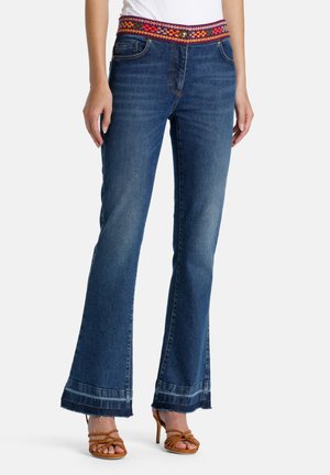 Jeans de denim acampanados con una cinturilla de tejido colorido, que presentan un lavado azul clásico, costuras visibles y detalles de dobladillo deshilachado.