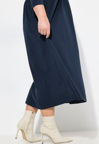 Lange marineblauwe jurk met lange mouwen, gecombineerd met witte hoge enkellaarsjes met een rits aan de zijkant. Glad stof en eenvoudig ontwerp.