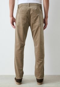 Khakifarbene Cordhosen im geraden Schnitt, mit zwei Gesäßtaschen und einer strukturierten Oberfläche. Getragen mit braunem Schuhwerk.