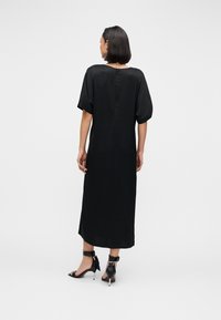 Schwarzes Midikleid mit kurzen Puffärmeln und geradem Schnitt. Verfügt über ein dezentes Rückenknopfdetail, kombiniert mit schwarzen Riemchenabsätzen.