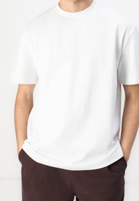 Valkoinen puuvillapaita, jossa on pyöreä kaula-aukko ja lyhyet hihat. Paidassa on rento istuvuus ja sileä, tasainen pinta. Ei näkyviä kuvioita tai yksityiskohtia.