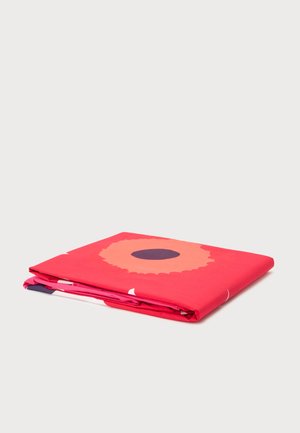 Tissu rouge vif plié avec un grand motif de fleur stylisée comportant un centre pêche et un cercle sombre au milieu, sur un fond blanc uni.
