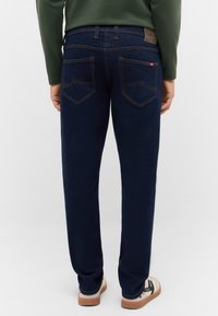 Ciemnoniebieskie jeansy z denimu z pomarańczowym przeszyciem, wyposażone w dwie tylne kieszenie z charakterystycznym wzorem szwów oraz brązową skórzaną naszywką na talii.