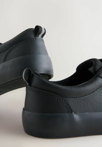 Zwarte rubberen schoenen met een glad leren bovenwerk, voorzien van een achterste trekkoord met zwart-witte strepen en subtiele stiksels.